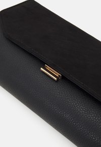 Borsa a mano nera con finitura testurizzata, dotata di una patta in suede e di un dettaglio della chiusura in tono oro. La forma complessiva è rettangolare.