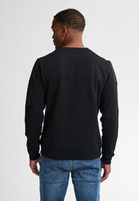 Zwarte sweatshirt met een geribde ronde hals en lange mouwen, gemaakt van textuurstof, in combinatie met blauwe jeans. Achteraanzicht weergegeven.