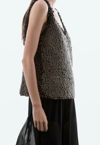 Grijs mouwloos topje met een getextureerd oppervlak met verhoogde, kiezelachtige details, gecombineerd met een zwarte, doorschijnende onderste laag.