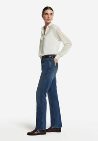 Vit, långärmad skjorta med knappar, blå raka jeans, mörkbrun bälte och loafers. Slätt tyg, klassisk passform och avslappnad stil.