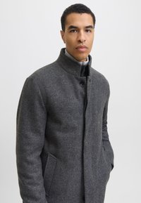 Hall villasegukangasest mantel kõrge kraega, ühe nupuga sulgemine, küljetaskud ja tekstuurse mustriga. Siseküljel kontrastne vooder.