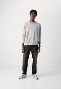 Sudadera de algodón gris con puños de canalé, jeans negros con textura desgastada y zapatillas de running plateadas con acentos y logo en negro.