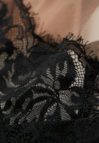 Czarna koronkowa tkanina z florystycznymi wzorami, z misternymi i teksturowanymi detalami na jasnobrązowym przezroczystym tle.
