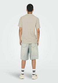 Camicia beige a maniche corte abbinata a pantaloncini di denim azzurro chiaro, caratterizzata da una vestibilità rilassata, tessuto testurizzato e tasche posteriori. Calzini a righe bianche e nere.