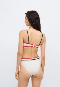 Σετ λευκό μπικίνι με κόκκινες και ναυτικές λεπτομέρειες. Ρυθμιζόμενοι ιμάντες, κλείσιμο με κούμπωμα στο πίσω μέρος, ψηλόμεσο κάτω μέρος. Λείο υλικό, μινιμαλιστικός σχεδιασμός.