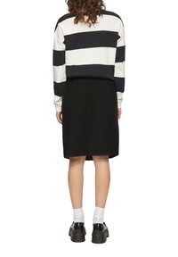 Abito nero con vita, abbinato a un maglione a strisce bianche e blu navy. L'outfit presenta maniche lunghe e scarpe nere robusta.