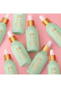Pixi Overnight Glow Serum-flasker, mintgrønne med gullfarger, med pipette-topper. Fire flasker arrangert på en rosa bakgrunn.