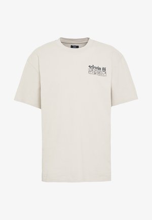 T-shirt en coton beige clair avec col rond, manches courtes, et un motif imprimé représentant des visages en noir sur le côté supérieur gauche.