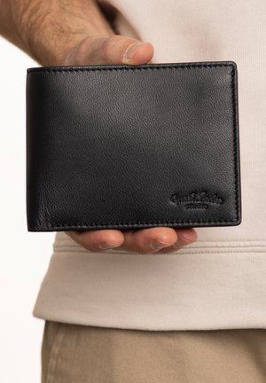 Black leather wallet held in a hand, featuring a smooth texture, straight edges, and embossed branding on the lower right corner.