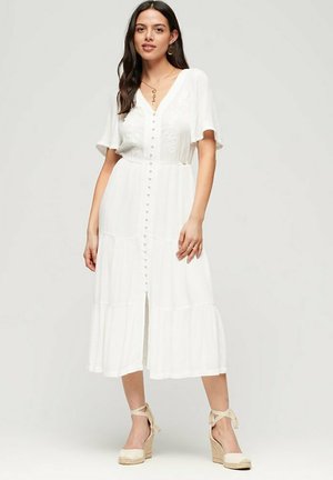 Vestido blanco de longitud a la rodilla con escote en V, mangas cortas, cierre de botones en la parte delantera y falda de capas. Tejido liso con un sutil bordado en el pecho.