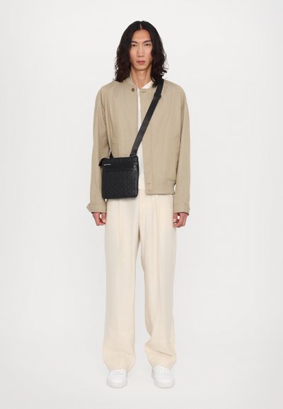 Veste légère beige, top crème et pantalon large crème. Sac à bandoulière noir avec un design matelassé et un détail de fermeture éclair. Baskets blanches.