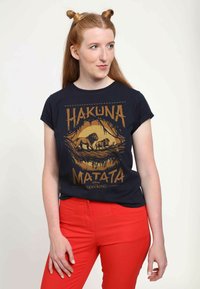 Černé bavlněné tričko s textem "Hakuna Matata" a zlatou grafikou lva. Krátké rukávy, volný střih, v kombinaci s červenými kalhotami.