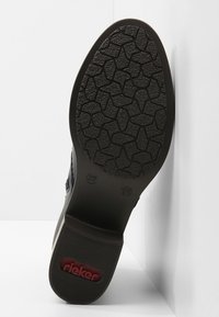 Suela de zapato Rieker que muestra una superficie de goma negra texturizada con un dibujo en relieve, con un logo rojo y una marcación de talla.