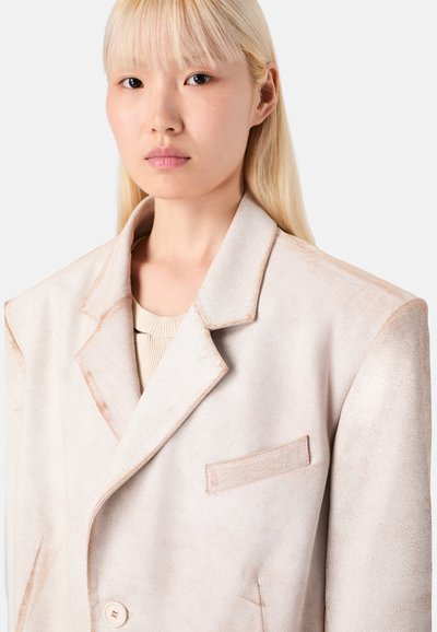 Helles beiges Oversized-Blazer mit strukturierter Oberfläche, Reverskragen, einreihiger Knopfverschluss und einer Brusttasche.