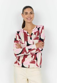 Langærmet top med henley-halsudskæring, lavet af blødt stof. Har et dristigt abstrakt mønster i nuancer af pink, rød og sort.