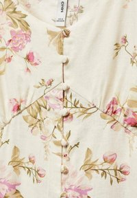 Robe florale en tissu crème ornée de motifs de fleurs roses et vertes, décolleté en V, et une rangée de boutons décoratifs blancs sur le devant.