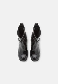 Paire de bottines noires brillantes à bouts carrés avec fermetures éclair latérales, vues de dessus sur un fond blanc.