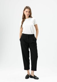 Wit nauwsluitend T-shirt gecombineerd met zwarte, op maat gemaakte broek met hoge taille en plooien, aangevuld met zwarte loafers met gouden accenten.