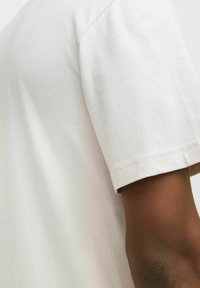 Tricou din bumbac de culoare bej deschis, cu mânecă scurtă, având un guler clasic, textură moale și cusături elegante pe mâneci.