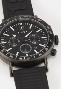 Reloj Timex negro con correa de silicona, con una esfera redonda, indicadores de horas blancos, taquímetro y subesferas para segundos y minutos.