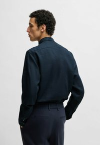 Granatowa, długosleeve koszula z lekkiego materiału, z kołnierzykiem typu band i zapinanymi mankietami, noszona z ciemnymi spodniami.