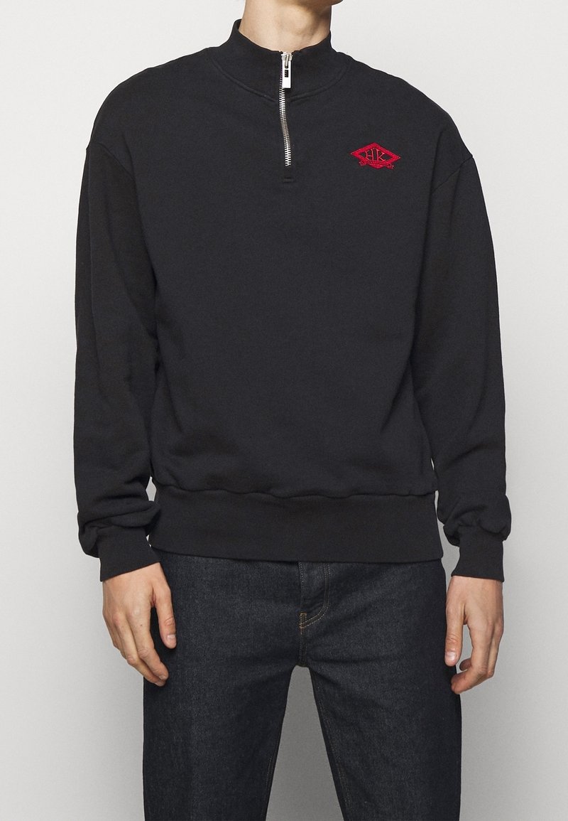 Black sweatshirt with high neckline and a quarter zipper. Features red embroidered logo on chest. Soft, textured fabric; ribbed cuffs and hem.