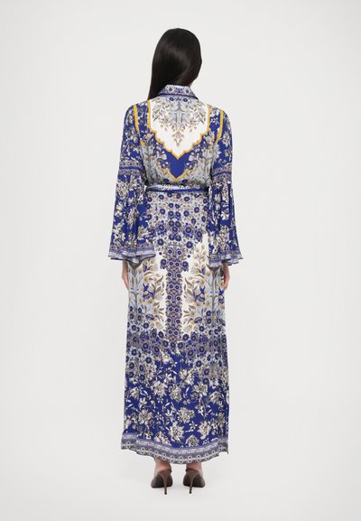 Robe longue bleue à fleurs avec des manches évasées, mettant en avant des motifs dorés et blancs élaborés, un col et un détail de taille nouée. Texture de tissu lisse.