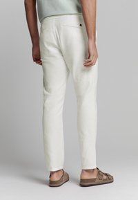Witte linnen broek met een slim fit, voorzien van een verborgen achterzak en subtiele textuur, gecombineerd met bruine sandalen met open teenn. 