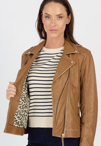 Braune Leder-Motorradjacke mit silberner Hardware, offen getragen, um ein Leopardenmuster-Futter zu zeigen, über einem gestreiften Pullover.