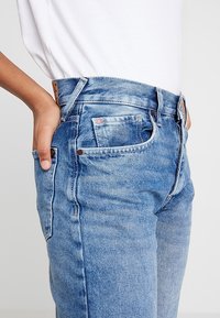 Ljust blå denimjeans med hög midja, femfickorsdesign och synlig sömnad. Tyget har en strukturerad yta med lätt blekning.