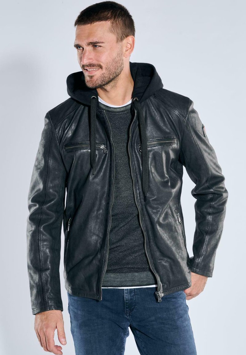 Black leather jacket with a zip front, two chest pockets, and hoodie-style neckline. Worn over a gray sweater and blue jeans.