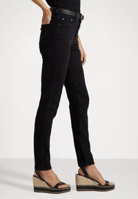 Zwarte denim skinny jeans met een hoge taille, voorzien van klassieke zakken en een strakke, gladde textuur. Gecombineerd met zwarte wedge sandalen.