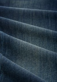 Denim tkanina u tamnoplavoj boji, sa mekanom teksturom, vidljivim uzorcima tkanja i suptilnim naglascima, koja pada u nabore.