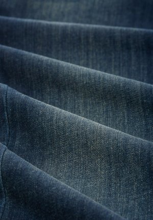 Tissu en denim bleu foncé, présentant une texture douce avec des motifs de tissage visibles et des reflets subtils, tombant en plis.