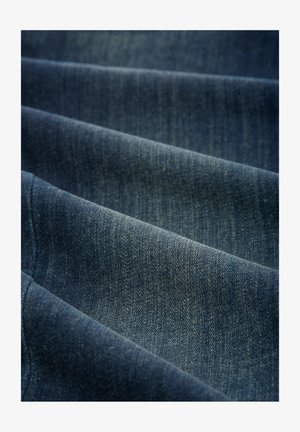 Tissu en denim bleu foncé, présentant une texture douce avec des motifs de tissage visibles et des reflets subtils, tombant en plis.