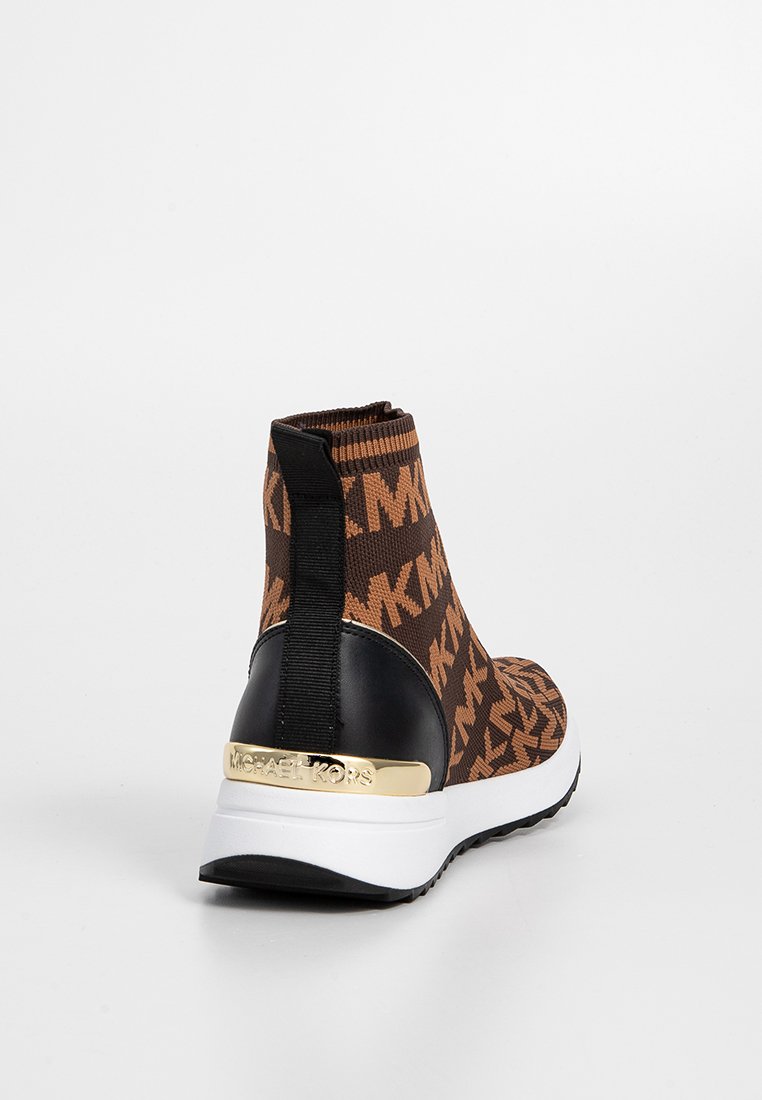 Zapatilla alta con tejido de punto marrón con patrón, talón negro, acento dorado de "Michael Kors", suela blanca y tirador negro en la parte trasera.