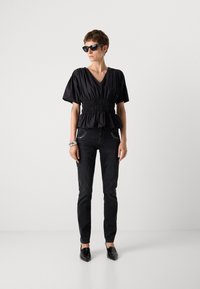 Crni peplum top s kratkim napušenim rukavima i naboranim strukom, uparen sa slim fit crnim trapericama i crnim štiklama sa šiljatim vrhom.