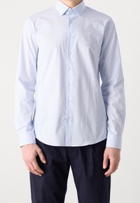 Camisa de botón de manga larga azul claro con finas rayas verticales, cuello puntiagudo y dobladillo redondeado. Presenta un logo en el pecho.