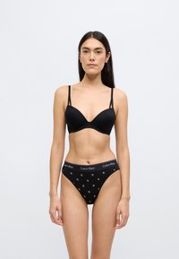 Μαύρο σουτιέν με ρυθμιζόμενες τιράντες, λείες κύπελλα, σετ με μαύρο εσώρουχο με σχέδιο που διαθέτει λωρίδα μέσης με λογότυπο και μικρές λεπτομέρειες με σήματα.