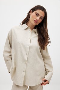 Camicia in lino beige con colletto, chiusura a bottoni e vestibilità ampia. Maniche lunghe con polsini piegati. Tessuto testurizzato.