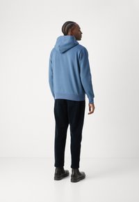 Felpa con cappuccio blu dal taglio rilassato, con tasca a marsupio, polsini e orlo ribattuti. Abbinata a pantaloni jogger scuri e stivaletti neri robusti.