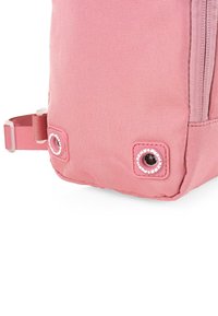 Mochila de tela rosa con una superficie texturizada, que presenta una correa lateral y dos acentos circulares con ojales en las esquinas inferiores para un detalle adicional.