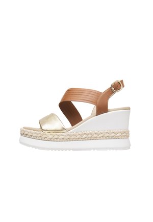 Sandalia de cuña con tira metálica dorada en el dedo, tira de cuero marrón en el tobillo, plataforma blanca y detalle trenzado de yute alrededor de la base.