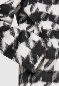 Zwart-wit houndstooth patroon jas met een zachte, pluizige textuur. Heeft een zichtbare zak en een schoon ontwerp op de mouw.