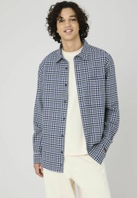 Chemise à carreaux bleu marine et blanche avec devant boutonné, col évasé, manches longues et poche poitrine, fabriquée dans un tissu léger.