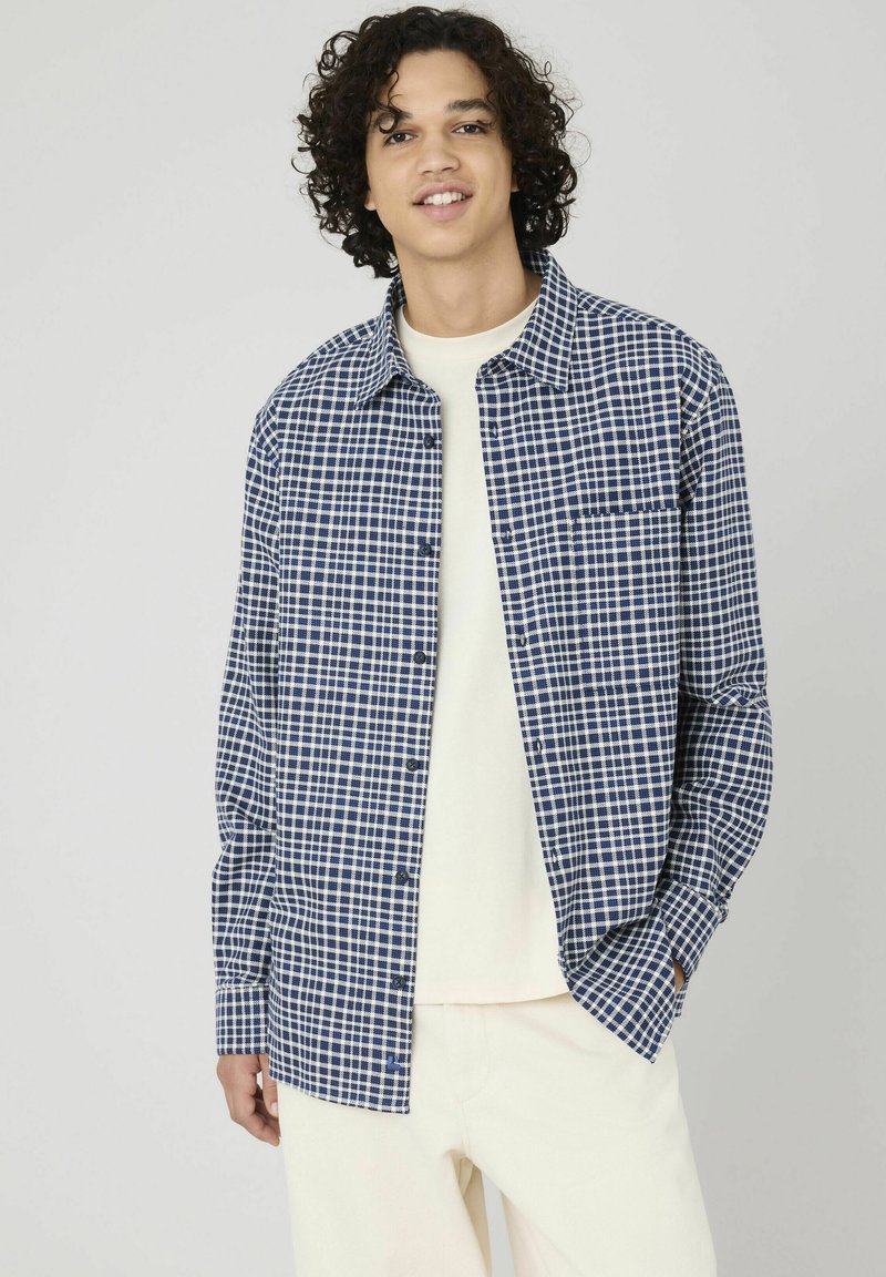 Chemise à carreaux bleu marine et blanche avec devant boutonné, col évasé, manches longues et poche poitrine, fabriquée dans un tissu léger.