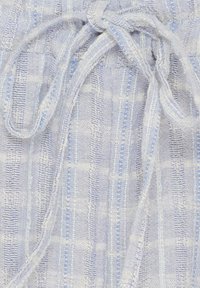 Lys blå stof med en tekstureret vævning, der har et subtilt ternet mønster og en båndlukning. Materialet ser blødt og letvægtsagtigt ud.