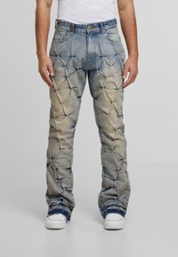 Jasnoniebieskie, teksturowane dżinsy z unikalnym pikowanym wzorem, o prostym kroju i postrzępionych brzegach. Noszone z białymi trampkami.