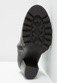 Bottine en cuir noir avec une semelle en caoutchouc, dotée d'un talon épais, d'un motif de grip texturé et d'un détail de fermeture éclair sur le côté.