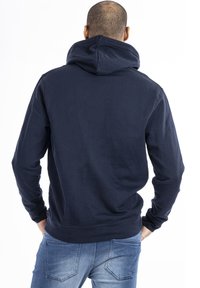 Mörkblå huvtröja med regular fit, ribbstickade muddar och nedkant. Mjuk textur och känguruficka, visad bakifrån.